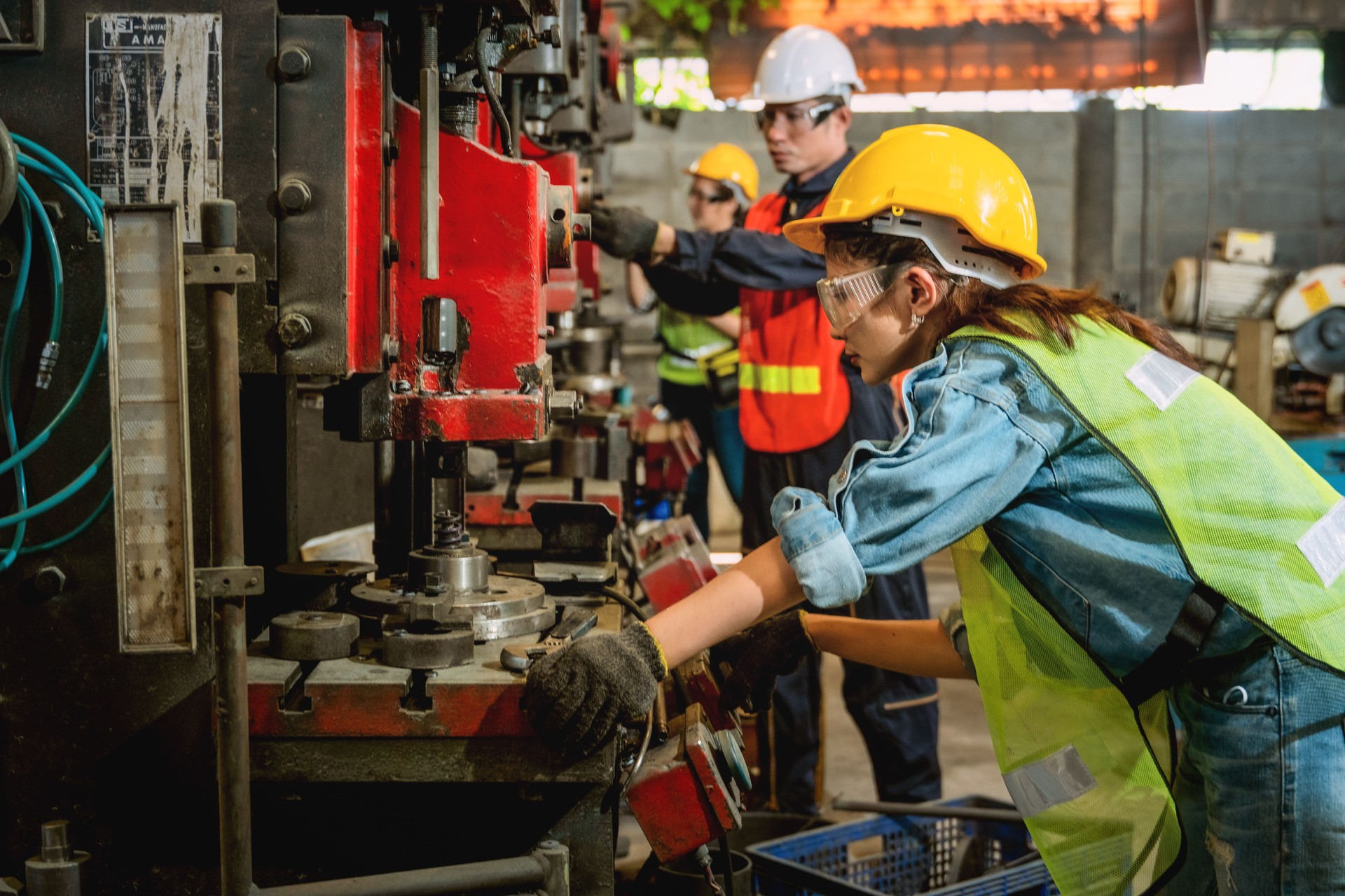 asian female and male manufacturing workers operating steel drilling machine together in line of metal work production factory